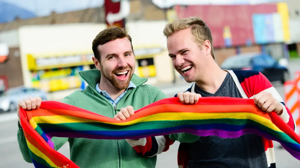 Two joyful men, holding a rainbow pride scarf, smiling outdoors. This represents the hope and inclusivity for gay and HIV-positive men pursuing fatherhood through IVF and surrogacy.