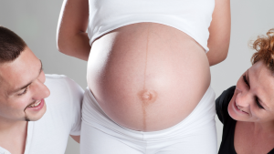 Intended parents smiling at pregnant surrogate’s belly, capturing the emotional bond and hope behind how long it takes to find a surrogate