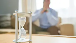 Hourglass on a table with a waiting intended parent in the background representing factors that affect surrogate matching time