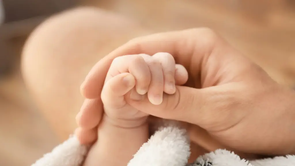 Newborn baby holding an adult’s finger representing the outcome of a surrogacy journey