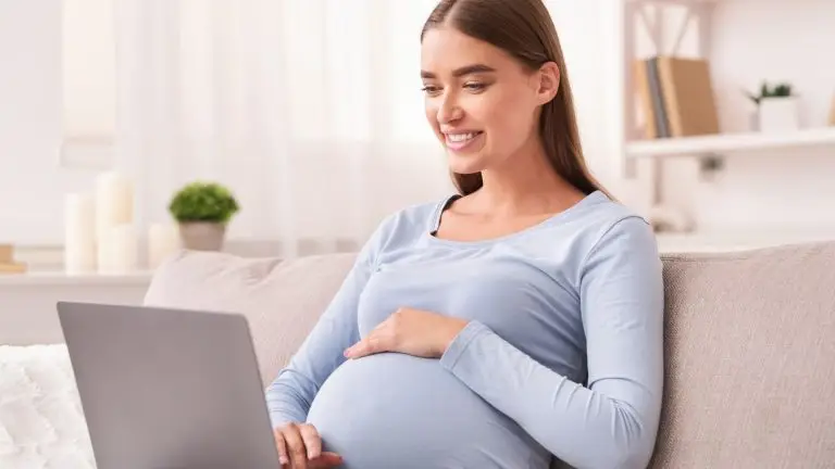 Pregnant surrogate reviewing surrogacy insurance information on a laptop at home