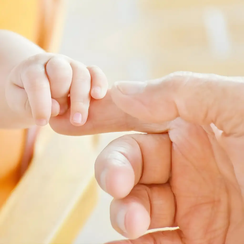 Parent gently holding newborn baby finger symbolizing surrogacy and family connection
