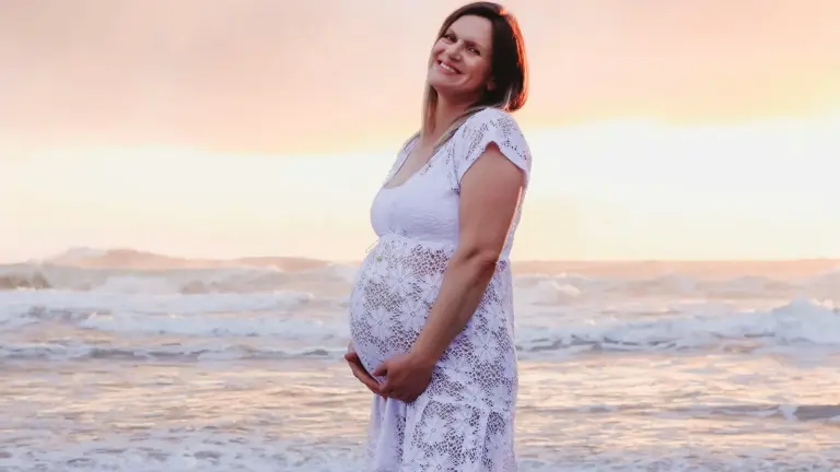 pregnant surrogate standing on beach in Florida smiling during surrogacy journey