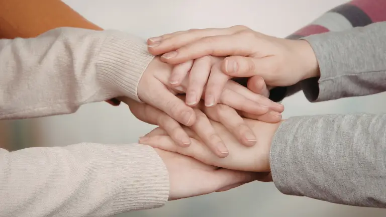 people placing hands together showing support and teamwork in a surrogacy journey