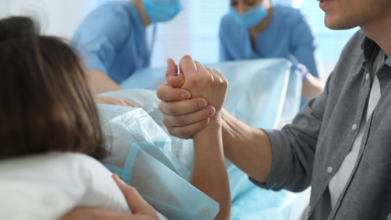 Surrogate holding a support person’s hand during delivery as medical staff assist in the hospital