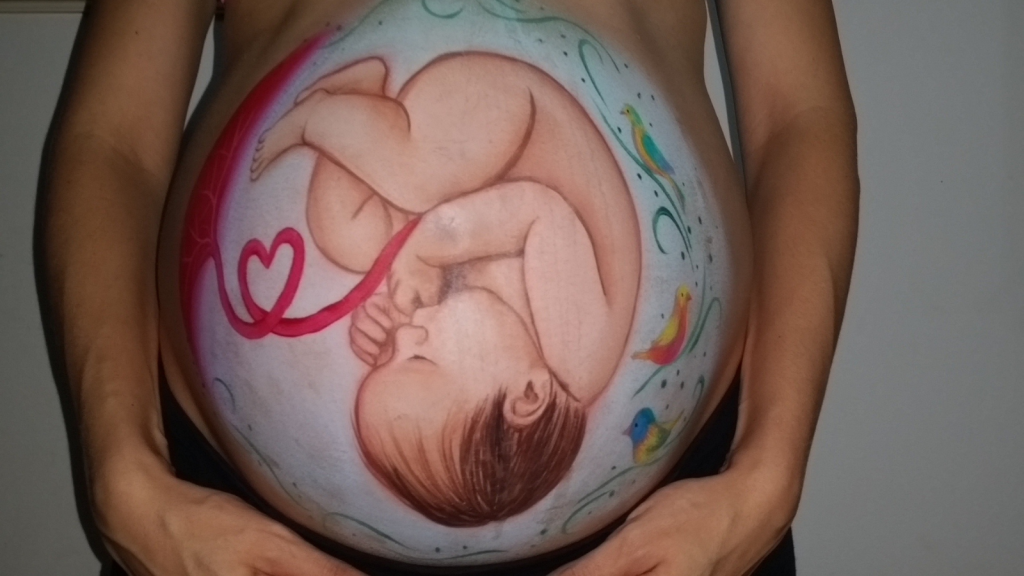 Pregnant belly painted with an illustration of a baby curled in the womb.