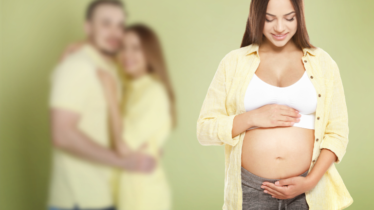Pregnant woman holding her belly with a couple in the background, illustrating an experienced surrogate considering another surrogacy journey.